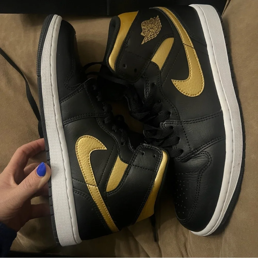 Nike Air Jordan 1 Mid in the black, metallic gold, and white colorway